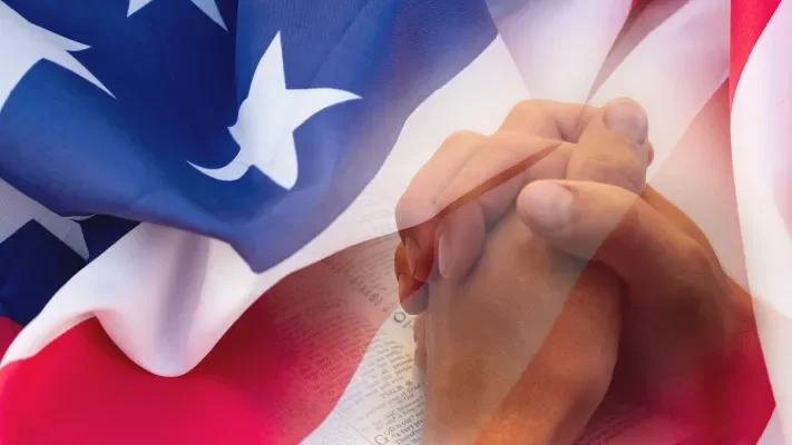 Praying hands representing Christian values over an American Flag