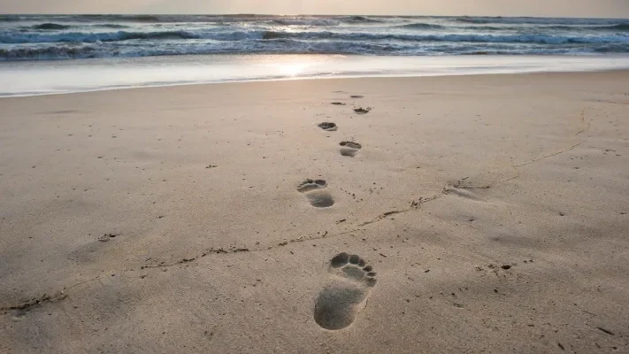 A pair of footprints walking across the sand representing following the teachings of Jesus.