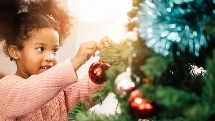 A young girl celebrates her Christmas spirit by hanging an ornament on the Christmas tree