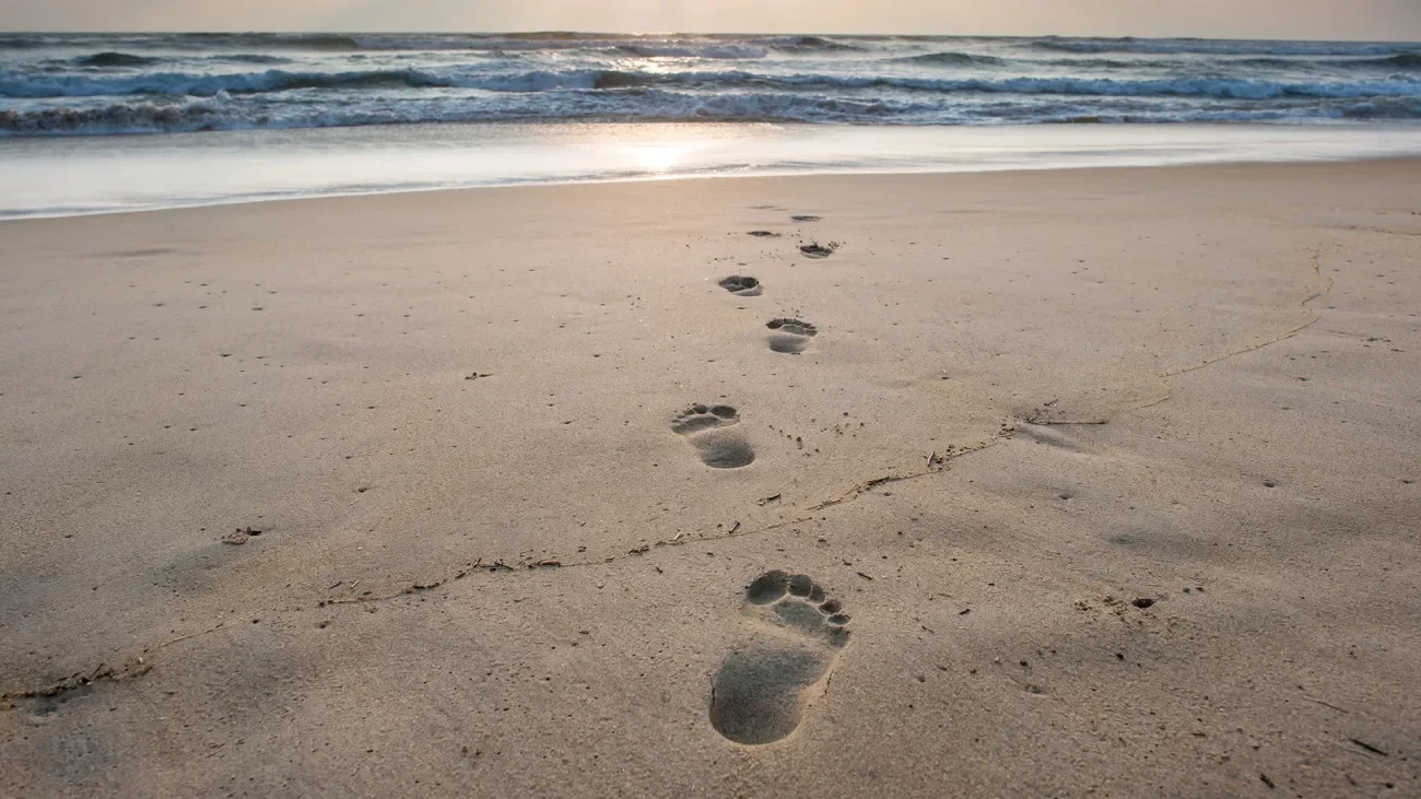 The Teachings Of Jesus: Love Beyond The Margins A pair of footprints walking across the sand representing following the teachings of Jesus.